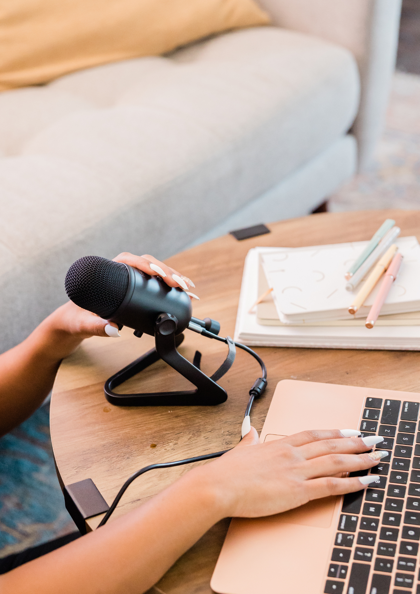 A black female holding onto a podcast mic with another hand on a laptop keyboard